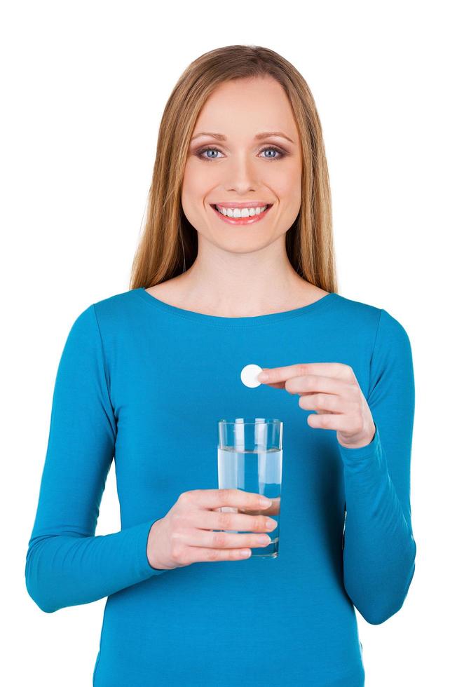 Heilpille. junge Frau, die eine Pille auf Glas mit Wasser hält, während sie auf Weiß isoliert steht foto