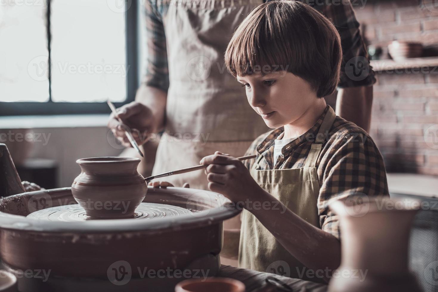 Freude am Töpferunterricht. kleiner Junge Zeichnung auf Keramiktopf im Töpferkurs foto