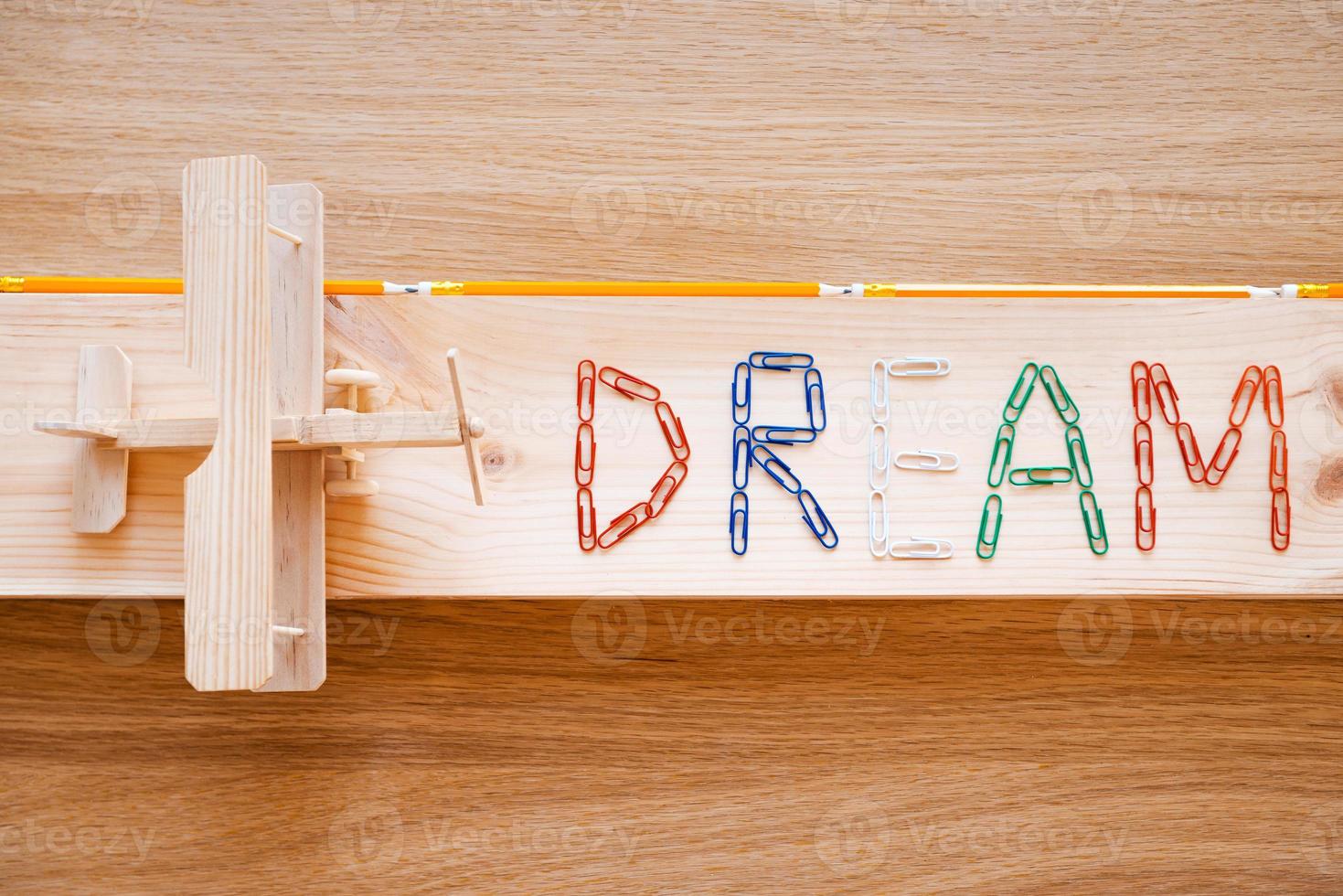 Träume werden wahr. Draufsicht auf Text aus bunten Heftklammern und Holzflugzeug, das auf die Holzmaserung gelegt wird foto
