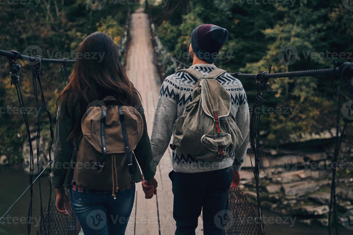 nächsten Schritt machen. Rückansicht des jungen Paares, das beim gemeinsamen Wandern im Wald auf die Hängebrücke tritt foto