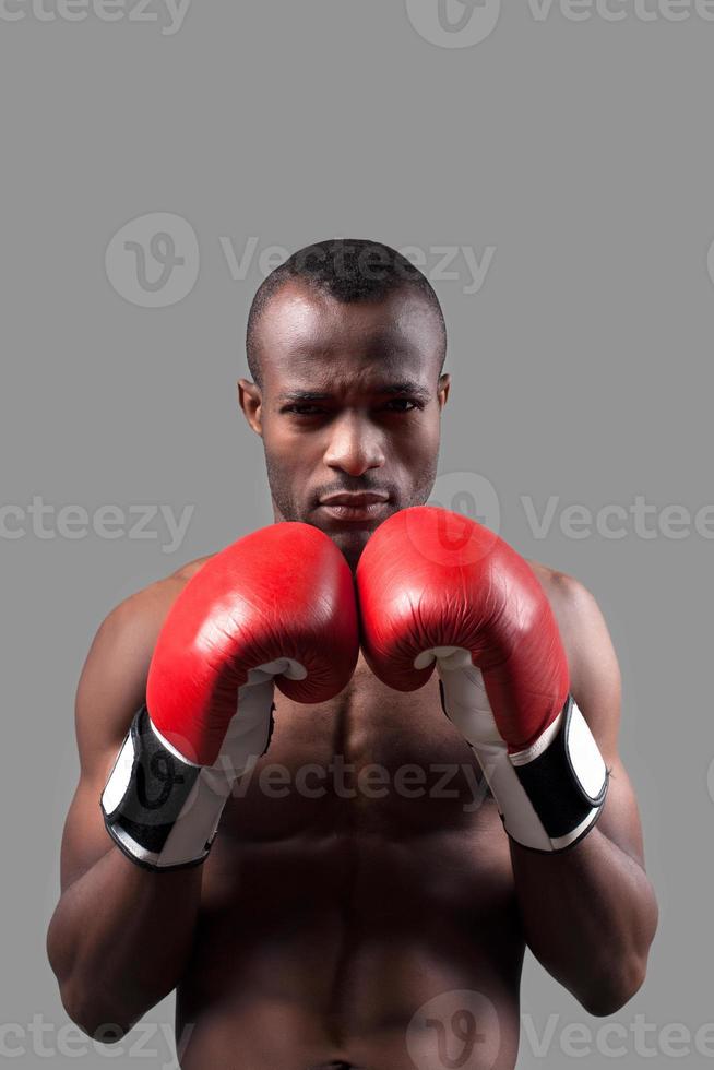 afrikanischer boxer. Selbstbewusster junger afrikanischer Boxer in Boxhandschuhen, der isoliert auf grau in die Kamera schaut foto