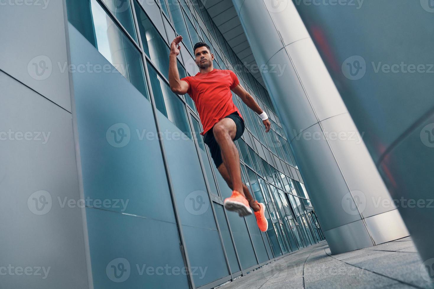 volle Länge eines starken jungen Mannes in Sportkleidung, der in der Luft schwebt, während er im Freien trainiert foto