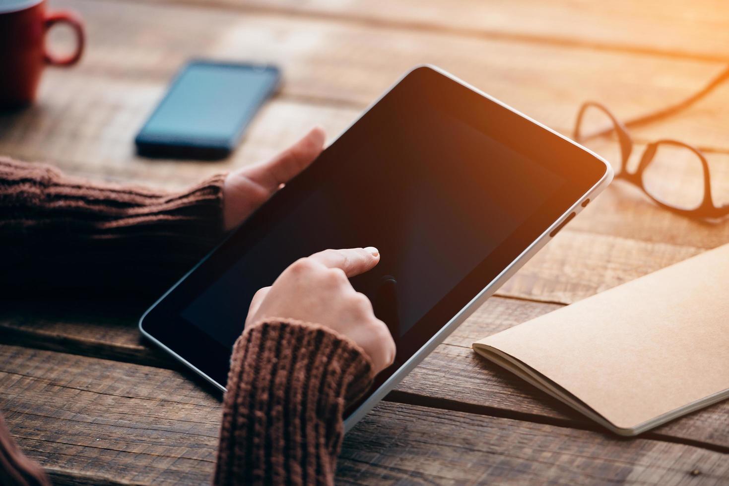 Öffnen Sie die Welt mit einer einzigen Berührung. Nahaufnahme einer jungen Frau, die ein digitales Tablet mit Kopienraum hält, während sie am rauen Holztisch sitzt foto