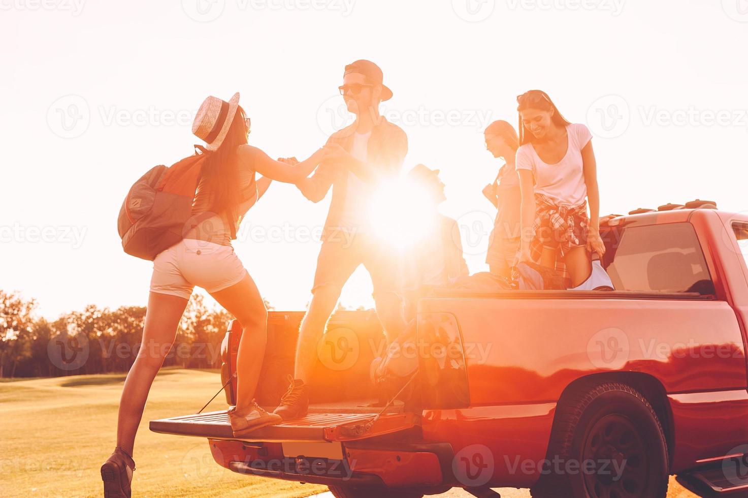 Vorbereitung auf einen großartigen Roadtrip. Schöne junge Leute bereiten sich auf einen Roadtrip vor, während ein fröhlicher Mann der Frau hilft, zum Pick-up-Truck zu gelangen foto