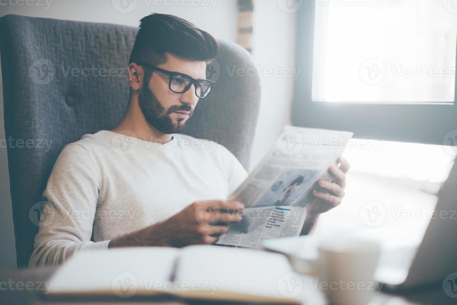 frische Zeitung lesen. Selbstbewusster junger Mann mit Brille, der Zeitung liest, während er im Büro oder Café sitzt foto