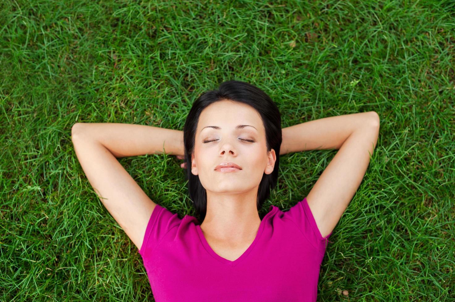 totale Entspannung. Draufsicht einer schönen jungen Frau, die schläft, während sie die Hände hinter dem Kopf hält und auf dem grünen Gras liegt foto