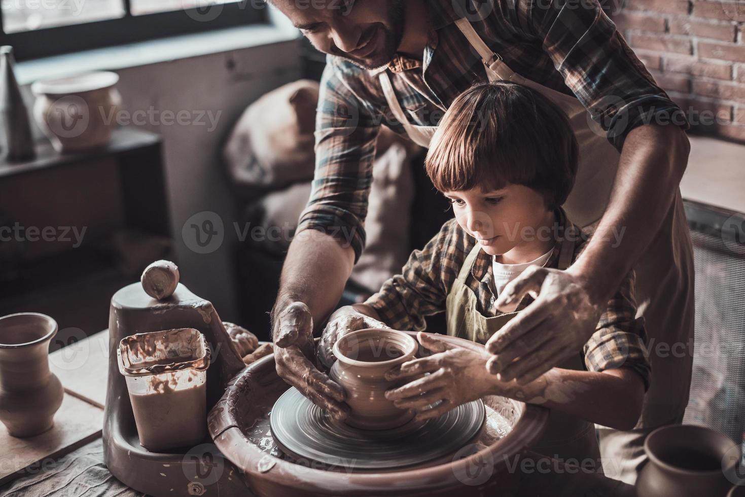 Erlernen neuer Fähigkeiten vom Töpfer. Blick von oben auf den fröhlichen jungen Mann und den kleinen Jungen, der Keramiktopf in der Töpferklasse herstellt foto