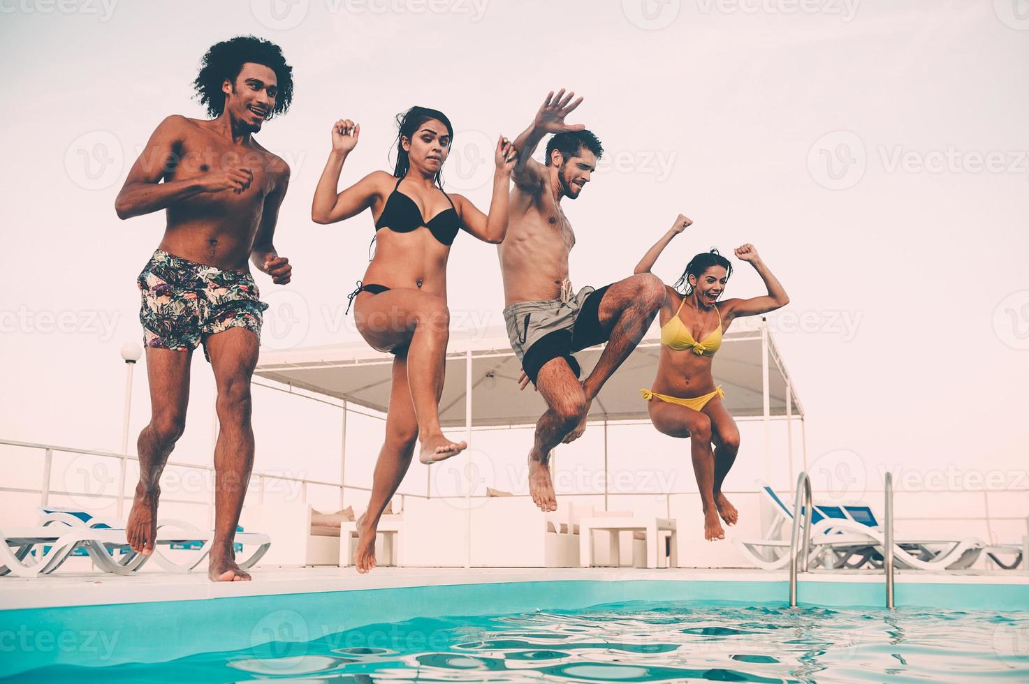 Zeit, sich zu erfrischen. Gruppe schöner junger Leute, die glücklich aussehen, während sie gemeinsam ins Schwimmbad springen foto