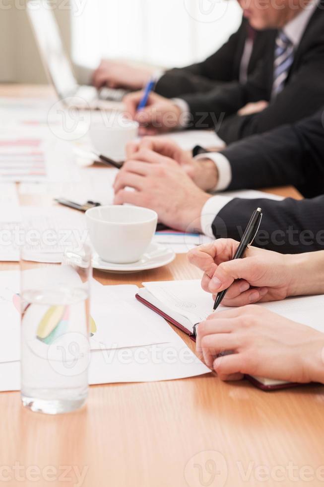 leute auf geschäftstreffen. Zugeschnittenes Bild von Menschen in formeller Kleidung, die zusammenarbeiten, während sie in einer Reihe am Tisch sitzen foto