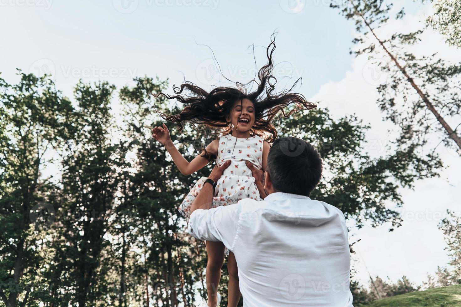 sie ist seine Prinzessin. junger liebevoller Vater, der seine lächelnde Tochter trägt, während er Freizeit im Freien verbringt foto