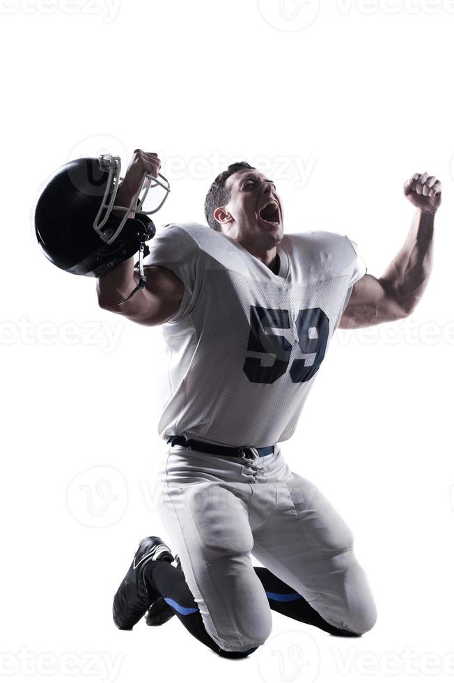 wilde Emotionen. American-Football-Spieler schreit und hält die Arme hoch, während er vor weißem Hintergrund kniet foto