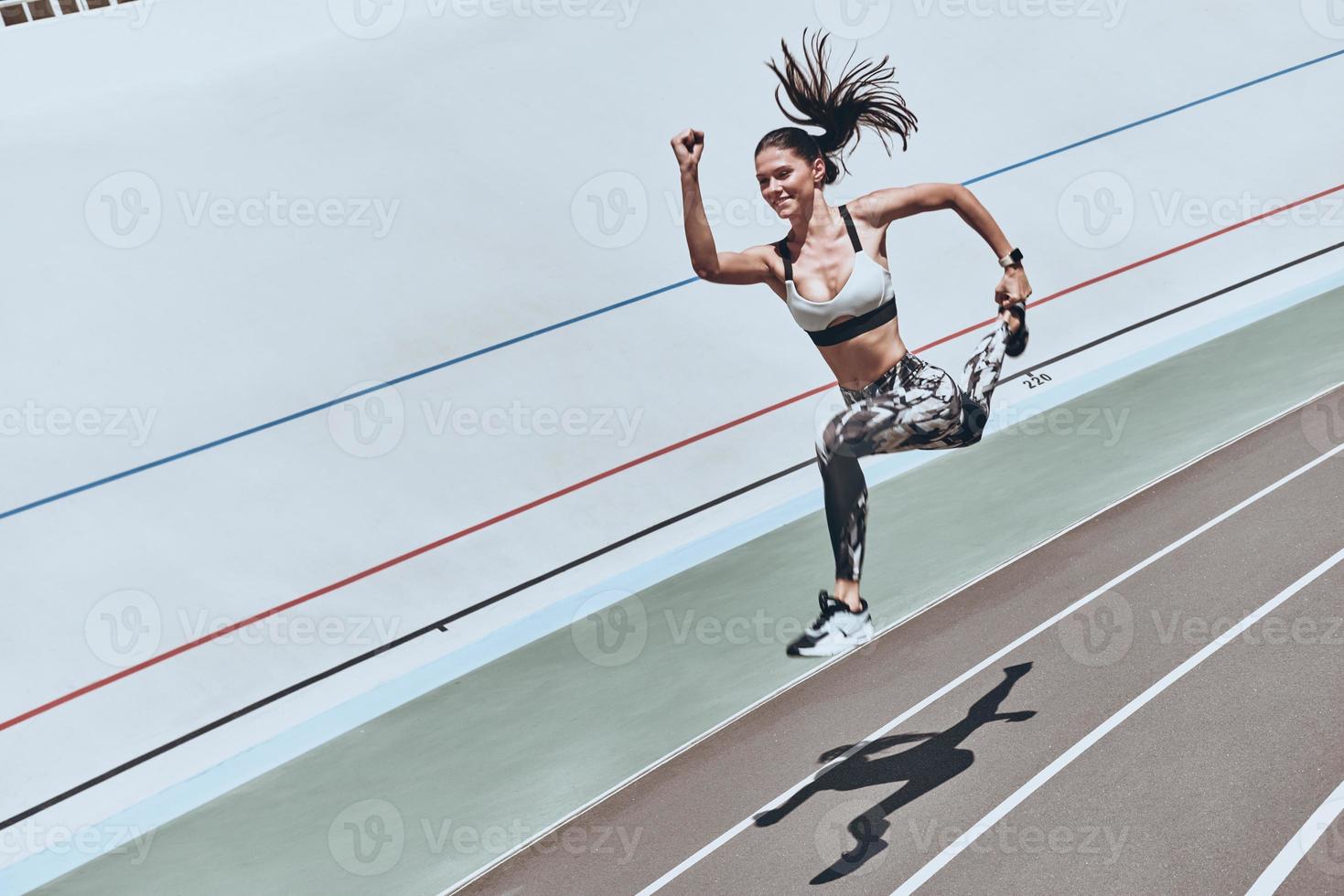 sich selbst herausfordert. Draufsicht einer jungen Frau in Sportkleidung, die springt und lächelt, während sie im Freien trainiert foto