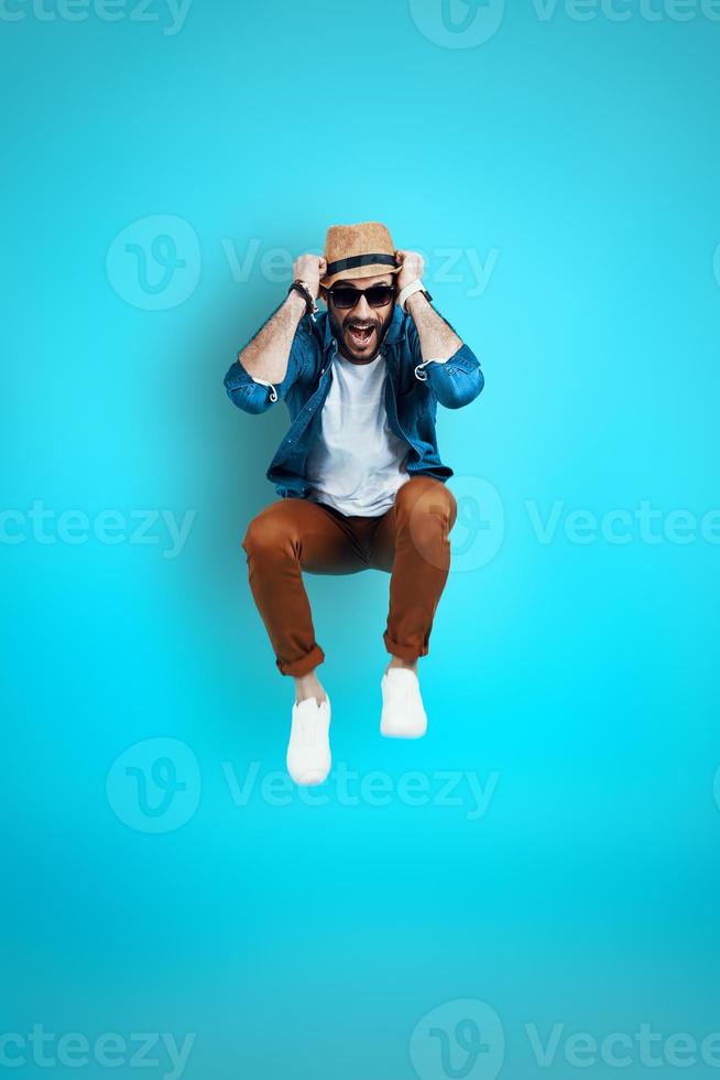 voller Länge von fröhlichen jungen Mann in Freizeitkleidung lächelnd im Stehen vor blauem Hintergrund foto