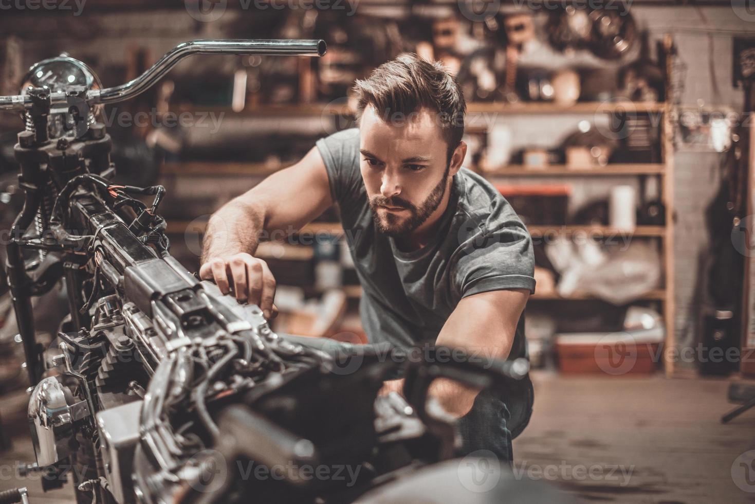 Fahrrad ist sein Leben. Selbstbewusster junger Mann, der Motorrad in der Werkstatt repariert foto