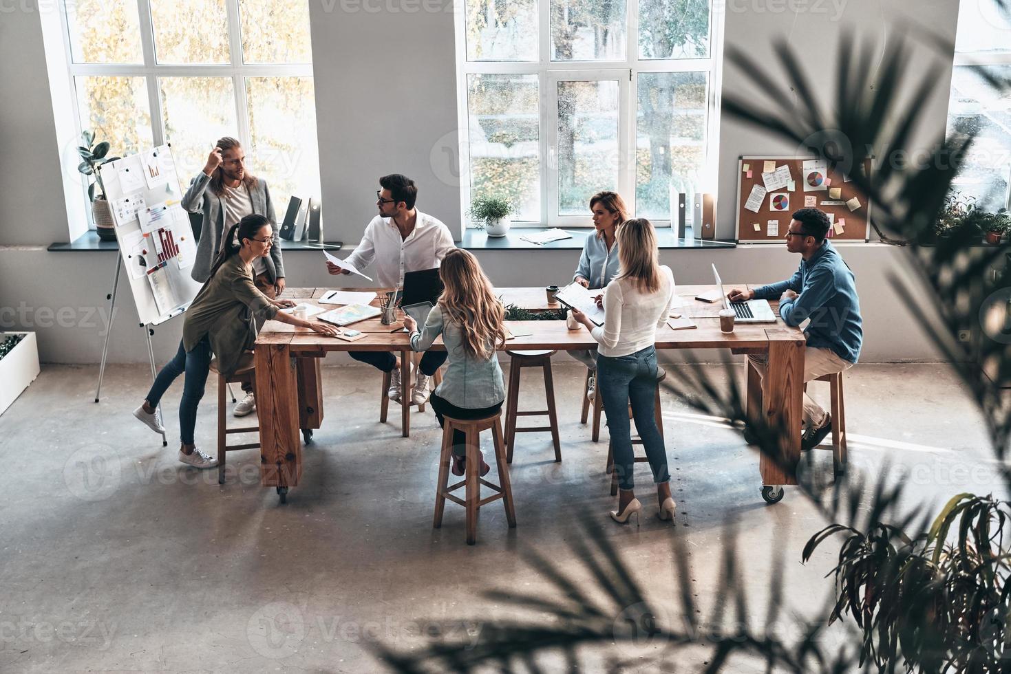 sich um das Geschäft kümmern. Draufsicht auf zwei moderne junge Kollegen, die eine Geschäftspräsentation durchführen, während sie im Sitzungssaal stehen foto