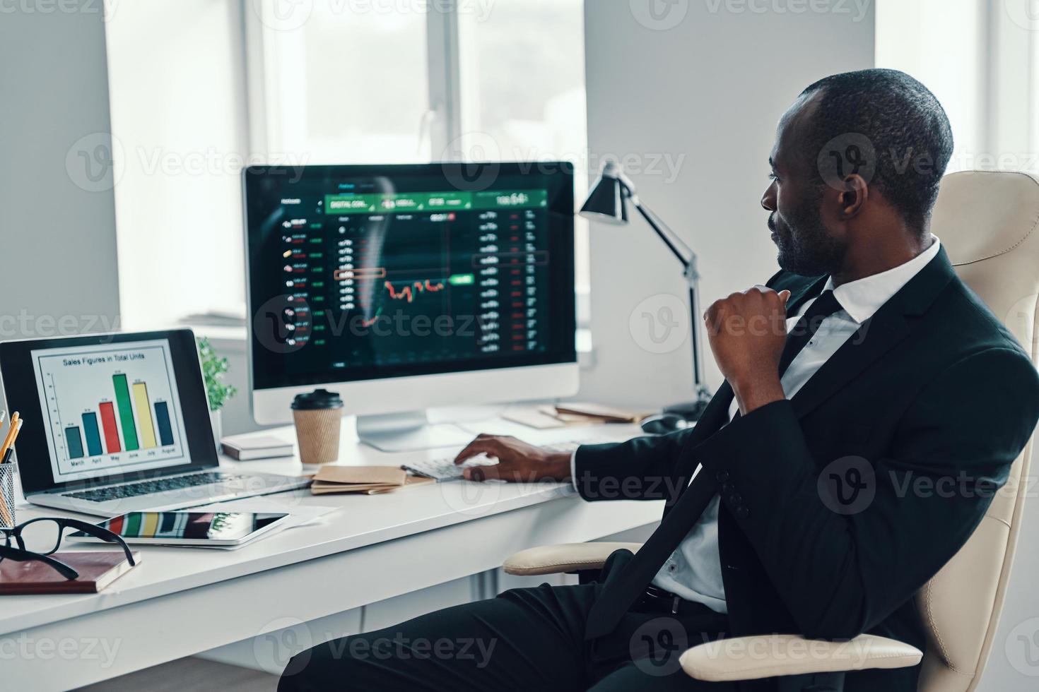 konzentrierter junger afrikaner in formeller kleidung, der moderne technologien einsetzt, während er im büro arbeitet foto