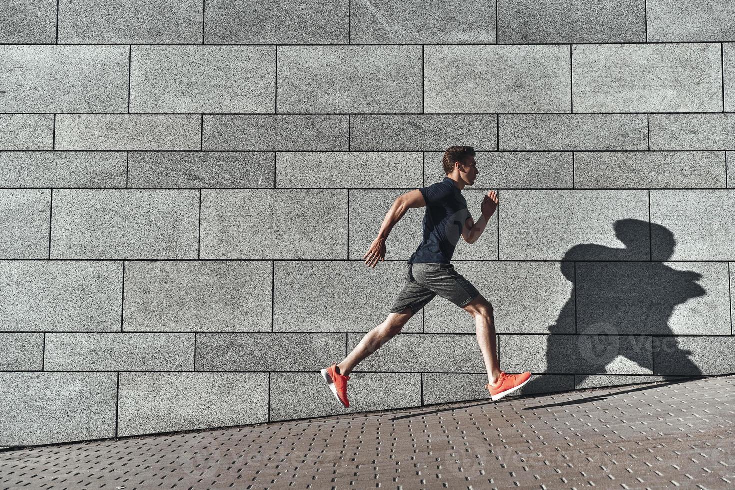 Morgentraining. Volle Länge des jungen Mannes in Sportkleidung, der beim Training draußen läuft foto