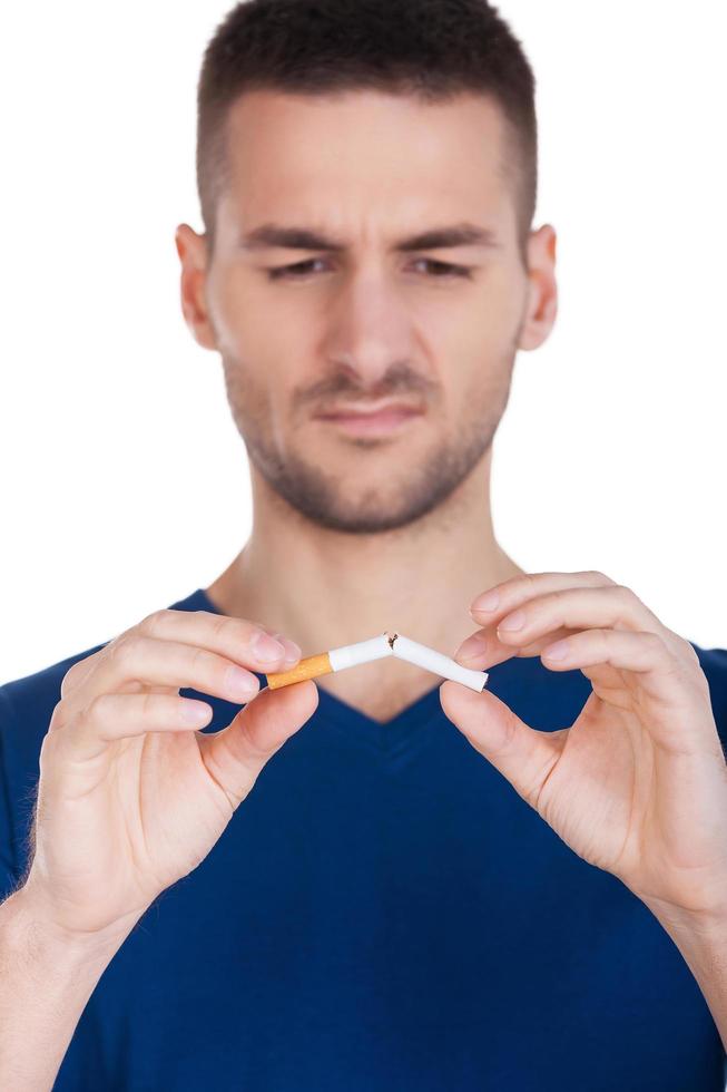 nicht mehr rauchen. ernsthafter junger Mann, der eine Schere in der Nähe der Zigarette hält, während er isoliert auf weißem Hintergrund steht foto