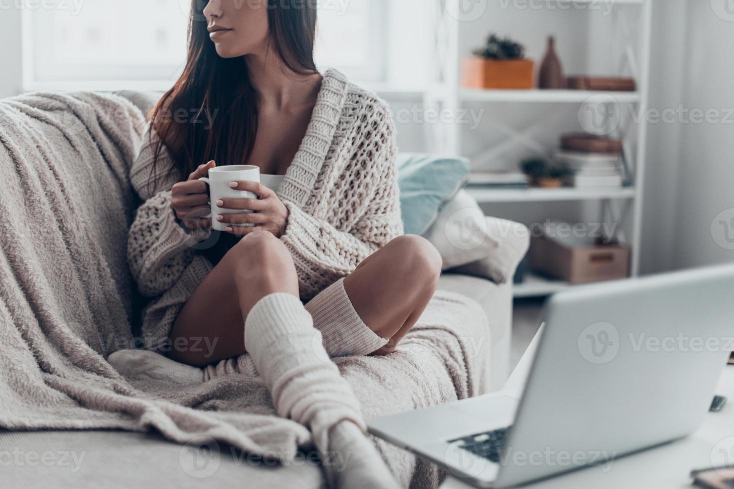 Morgenkaffee genießen. Nahaufnahme einer schönen jungen Frau, die eine Tasse hält, während sie sich zu Hause auf der Couch entspannt foto