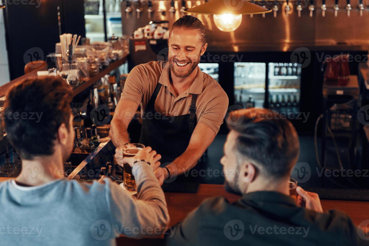 Blick von oben auf den Barkeeper, der jungen Männern Bier serviert, während er an der Bartheke im Pub steht foto