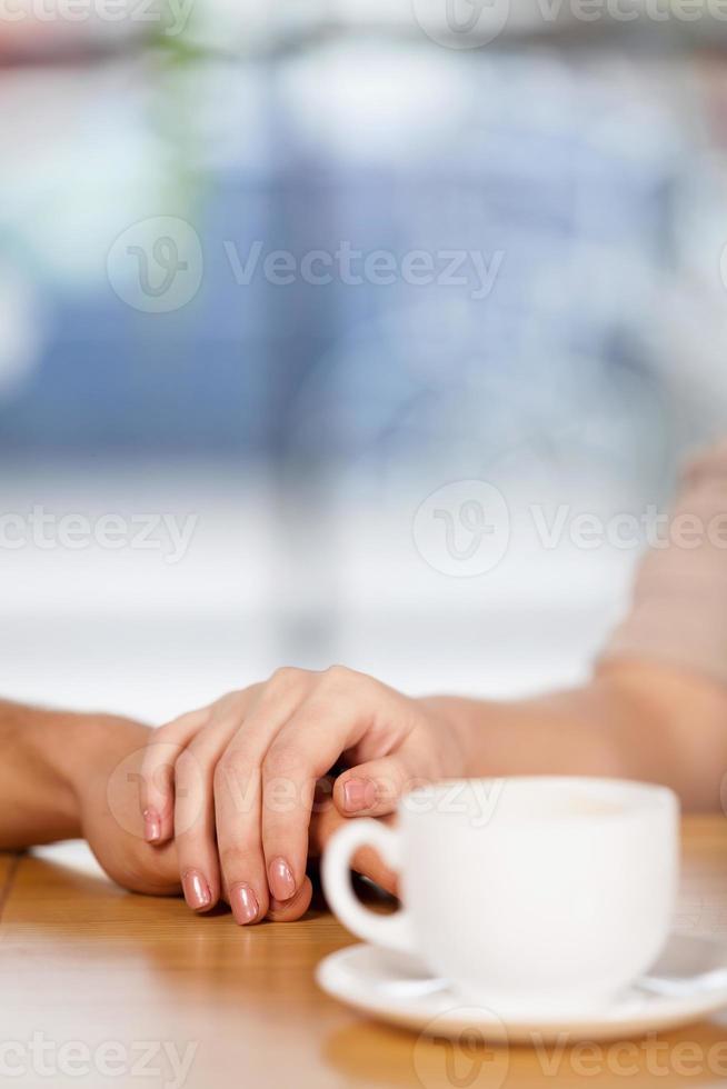romantischer Augenblick. Nahaufnahme eines Paares, das Händchen hält, mit einer Tasse Kaffee im Vordergrund foto
