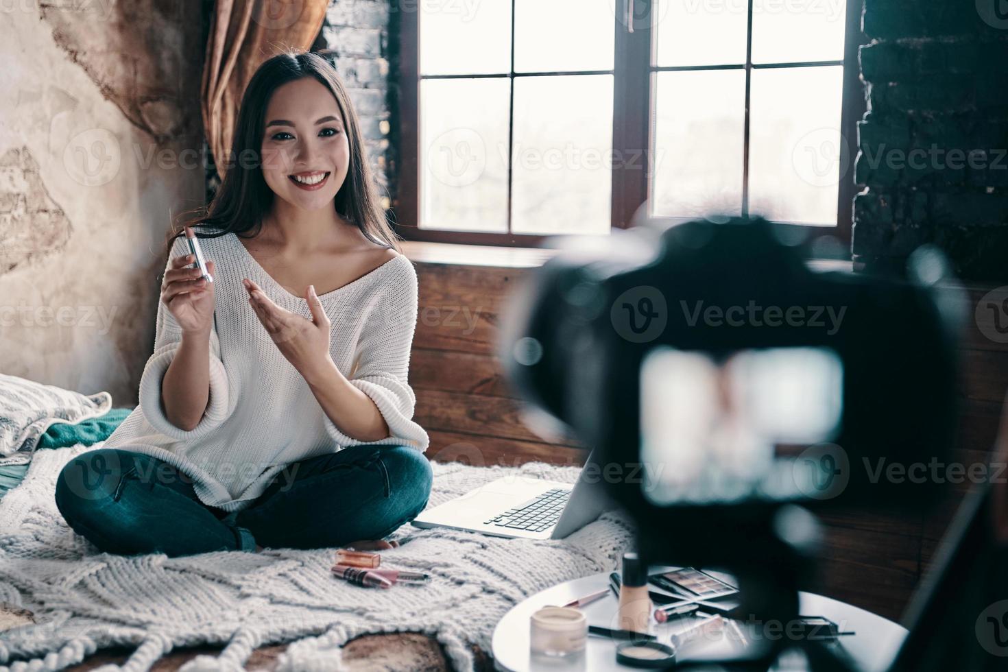 Produktvorteile teilen. schöne junge frau, die lippenstift hält und lächelt, während sie social-media-videos macht foto