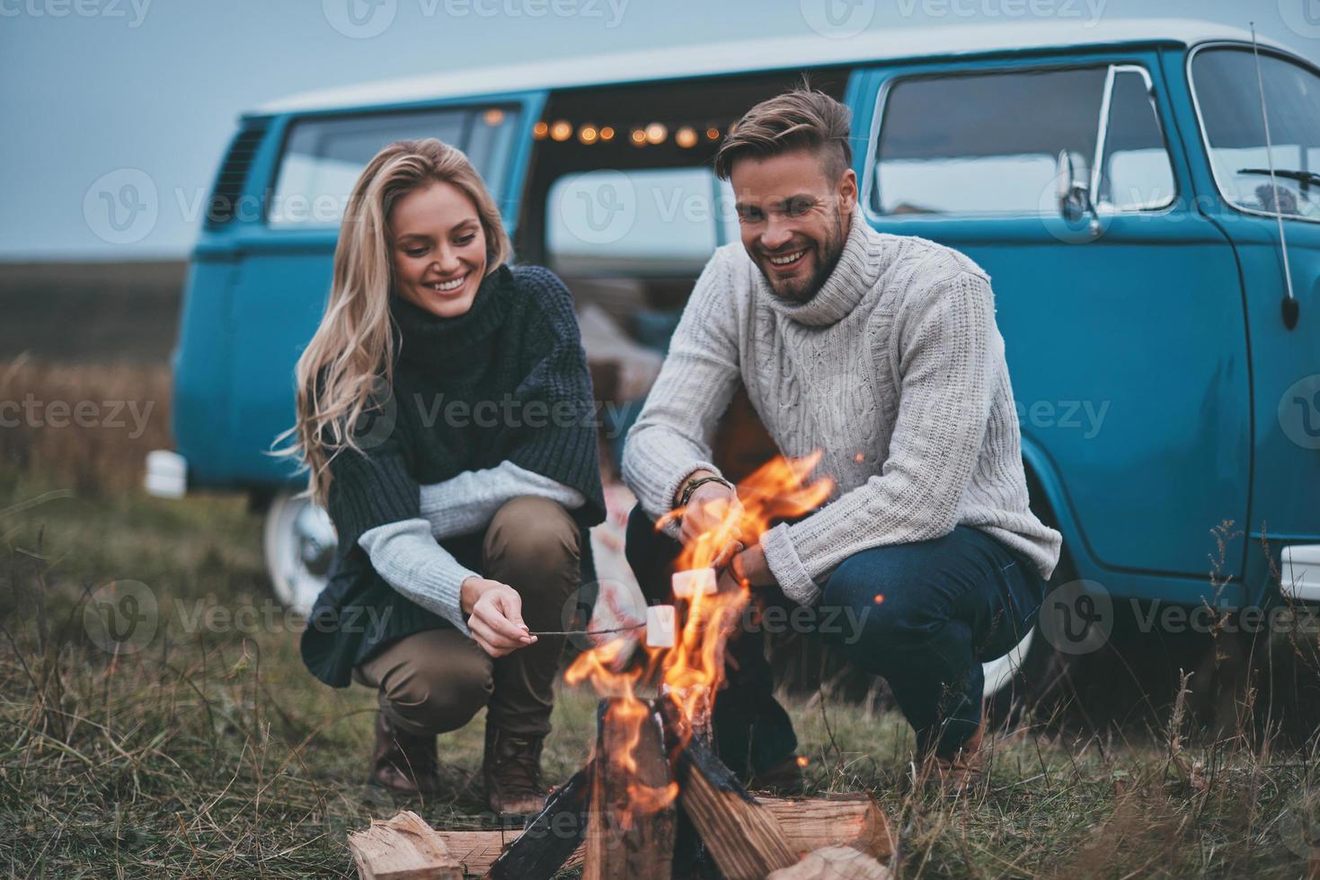 Genießen Sie eine großartige Reise zusammen. Schönes junges Paar, das Marshmallows über einem Lagerfeuer röstet, während es seine Straßenreise genießt foto