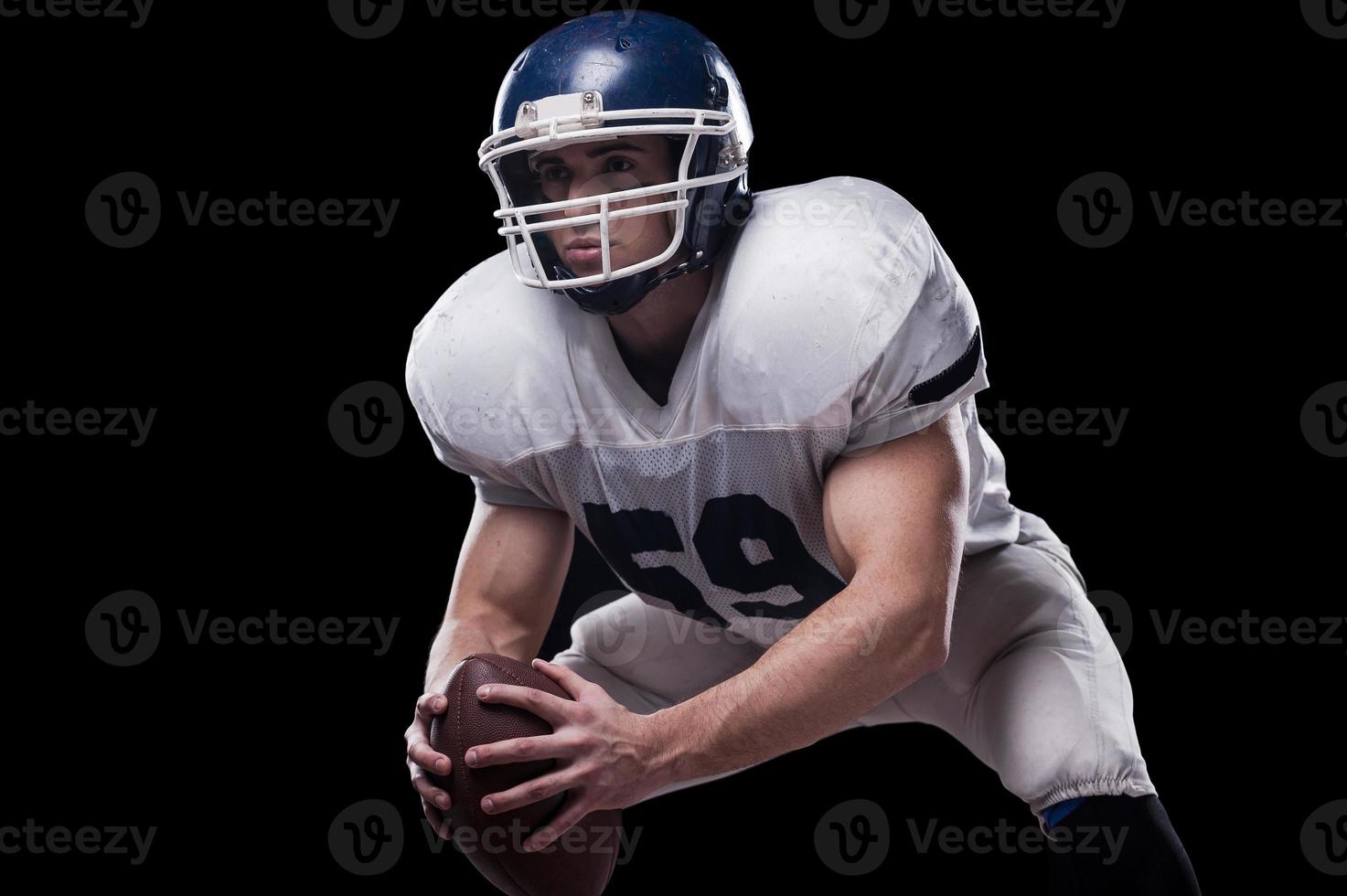 sich bereit machen, um dieses Spiel zu kämpfen. amerikanischer Fußballspieler, der Ball hält und wegschaut, während er vor schwarzem Hintergrund steht foto