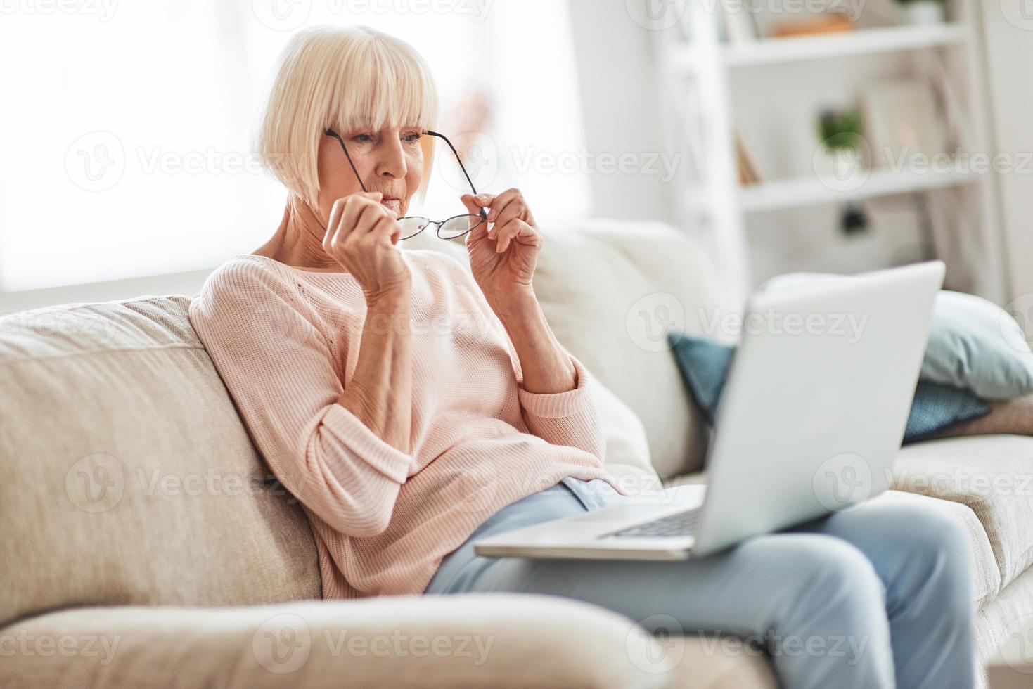 moderne Oma. Schöne Seniorin, die ihre Brille aufsetzt, während sie sich zu Hause auf der Couch entspannt foto