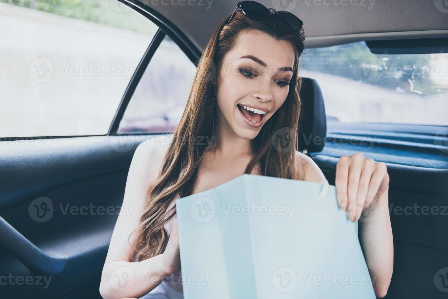 was für ein schönes kleid schöne junge lächelnde frau, die in die einkaufstasche schaut und überrascht aussieht, während sie im auto sitzt foto