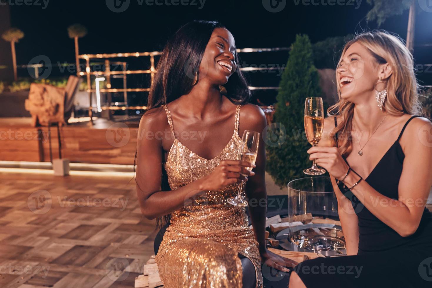 Zwei schöne Frauen in Cocktailkleidern kommunizieren und lächeln, während sie Zeit auf einer Luxusparty verbringen foto