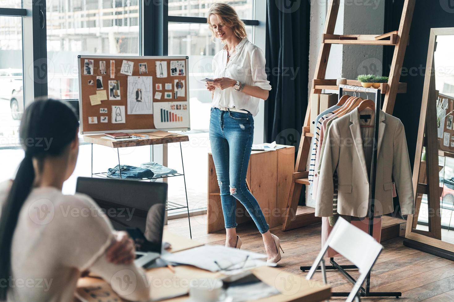 guten arbeitstag. Schöne junge Frau, die eine Geschäftsnachricht eingibt, während sie mit ihrem Partner in der Werkstatt zusammenarbeitet foto