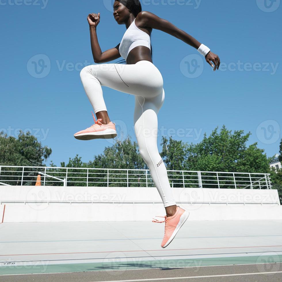 Selbstbewusste junge Afrikanerin in Sportkleidung, die im Freien auf die Strecke springt foto