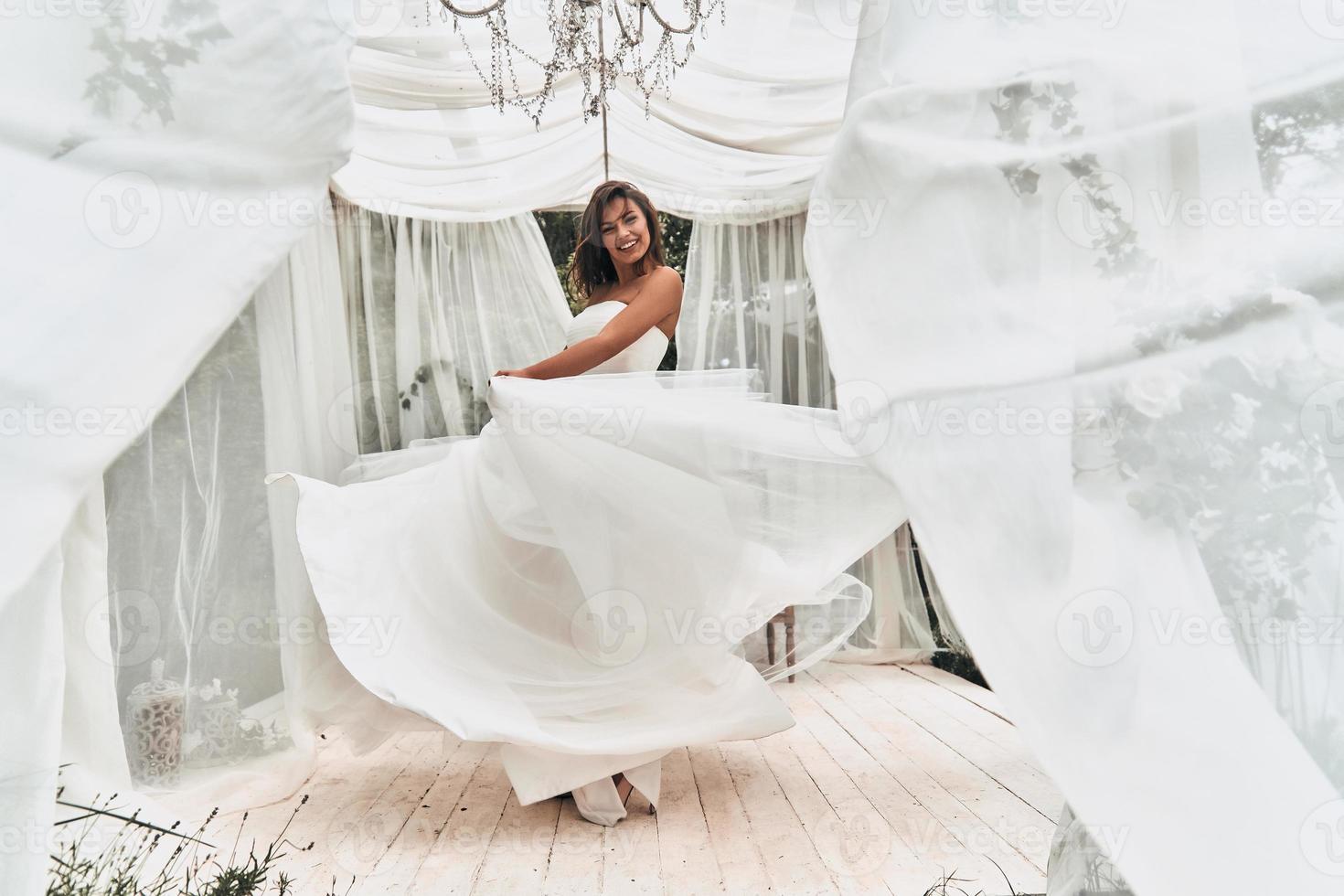 glücklich verheiratet zu sein. in voller Länge von der attraktiven jungen Frau im Hochzeitskleid, die beim Tanzen im Hochzeitspavillon draußen lächelt foto