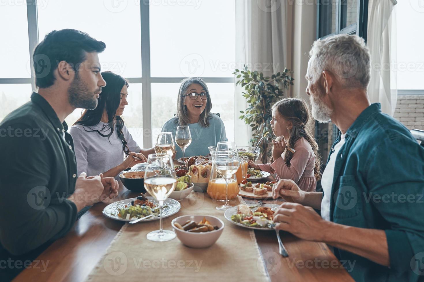 Lächelnde Familie mit mehreren Generationen, die beim gemeinsamen Abendessen kommuniziert foto
