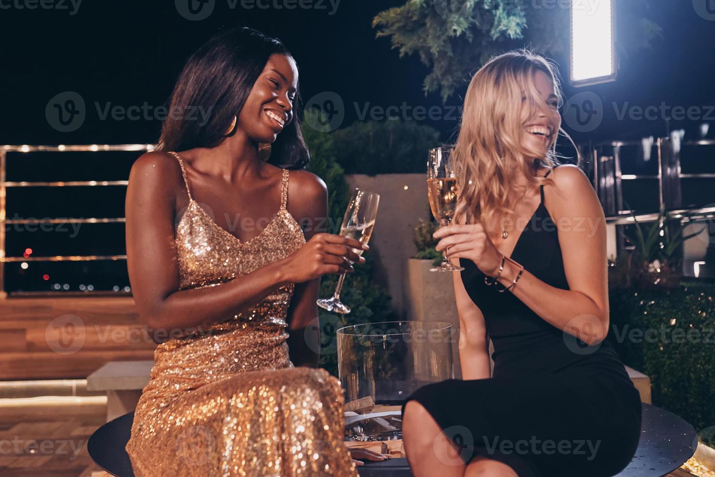zwei schöne frauen in abendkleidern kommunizieren und lächeln, während sie zeit auf einer luxusparty verbringen foto
