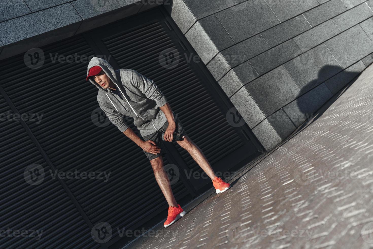 Zeit zum Ausruhen nehmen. Ganzkörperansicht eines jungen Mannes in Sportkleidung, der sich entspannt und wegschaut, während er draußen steht foto