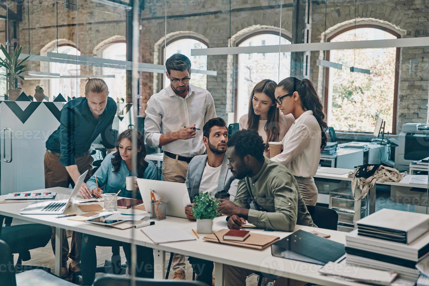 Gruppe junger moderner Menschen in eleganter Freizeitkleidung, die bei der Arbeit im Büro kommunizieren und moderne Technologien nutzen foto