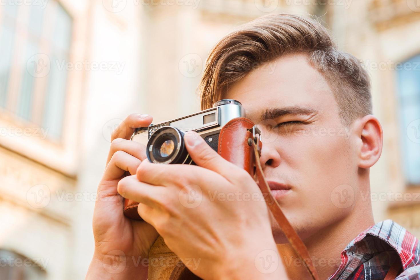 Moment einfangen. Tiefwinkelansicht eines hübschen jungen Mannes, der mit seiner Vintage-Kamera fotografiert, während er im Freien steht foto