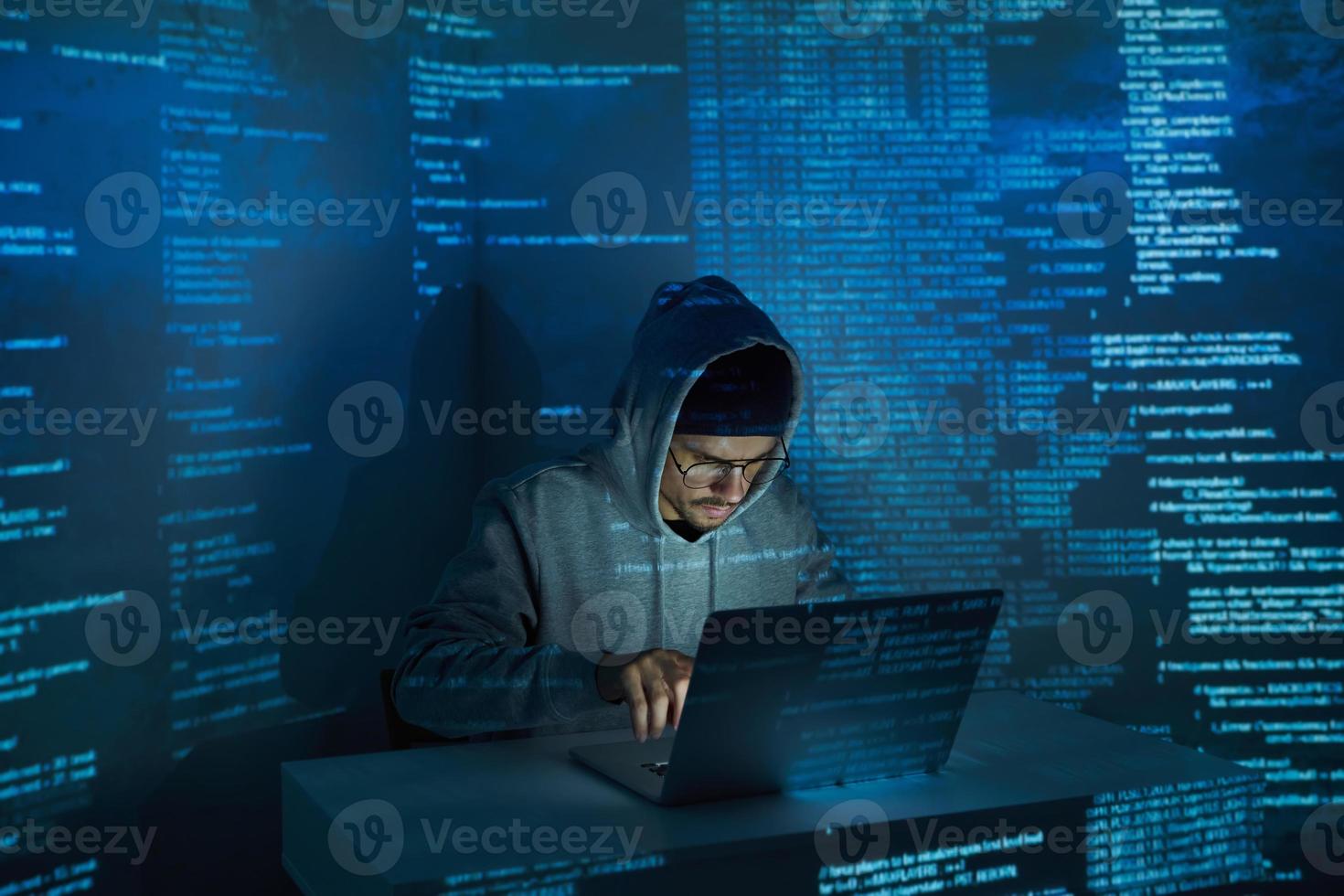 Selbstbewusster junger Mann im Kapuzenhemd mit Computer vor dunklem Hintergrund foto