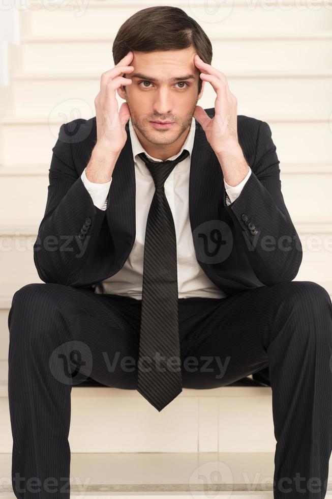 depressiver Geschäftsmann. Depressiver junger Mann in Abendkleidung, der den Kopf in der Hand hält und wegschaut, während er auf der Treppe sitzt foto