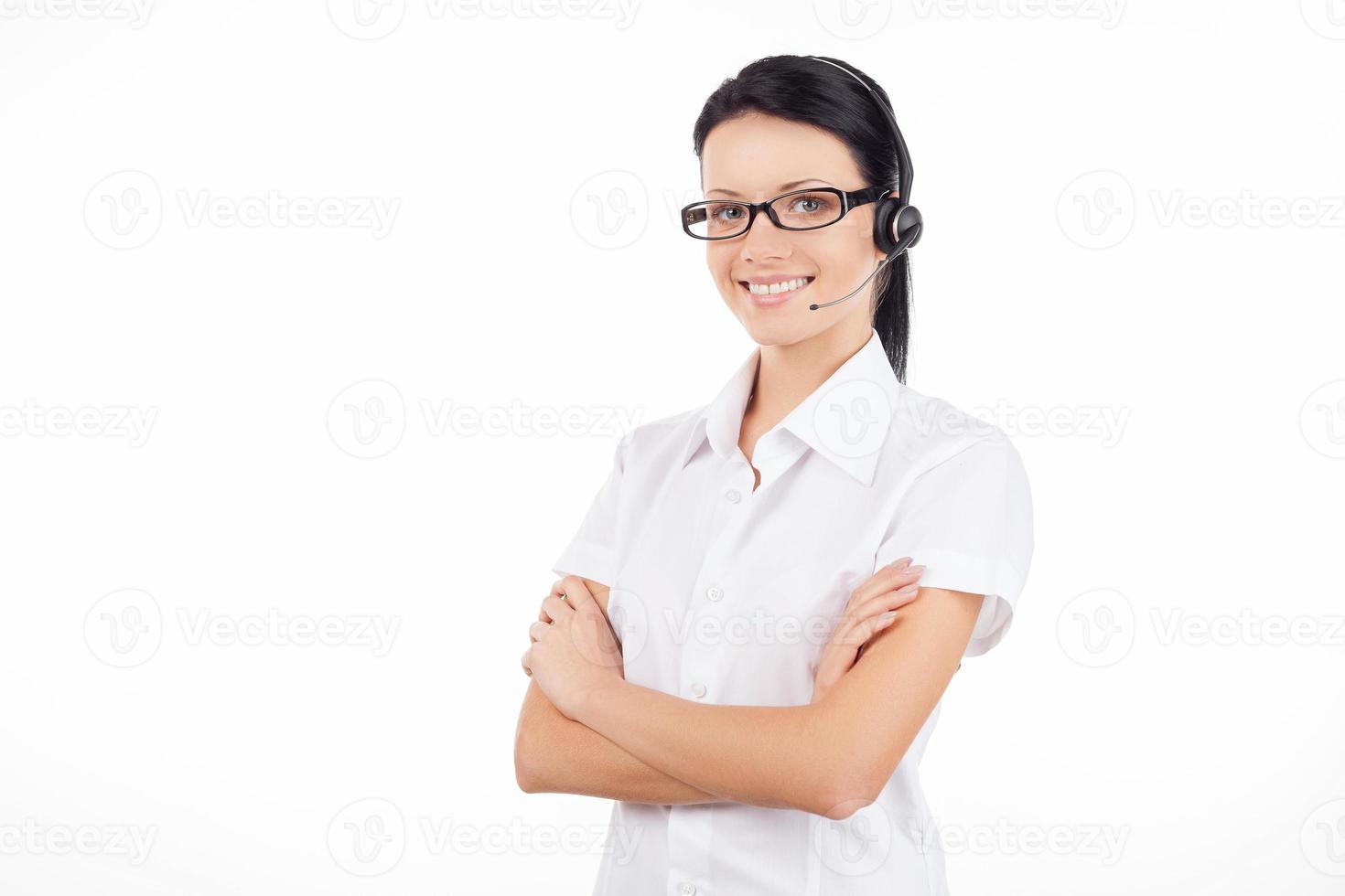 Kundendienstvertretung. Selbstbewusste junge Frau mit Headset, die lächelt und ihre Arme verschränkt hält, während sie isoliert auf Weiß steht foto