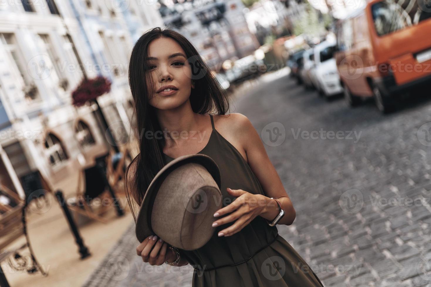 bestes Sommeraccessoire. attraktive junge frau, die ihren hut hält, während sie draußen steht foto