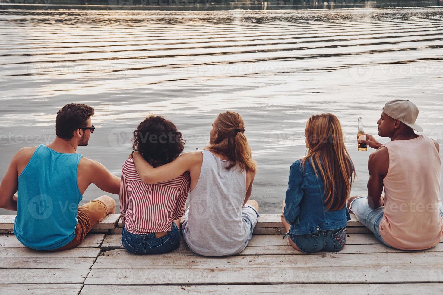 machen was sie wollen. Rückansicht junger Menschen in Freizeitkleidung, die sich unterhalten, während sie auf dem Pier sitzen foto