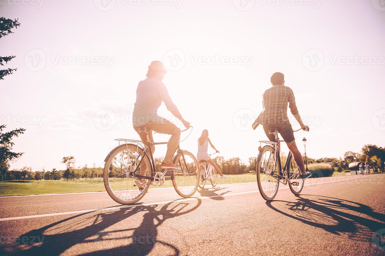 unbeschwerte gemeinsame Zeit genießen. Rückansicht junger, fröhlicher Menschen, die gemeinsam auf einer Straße Fahrrad fahren foto