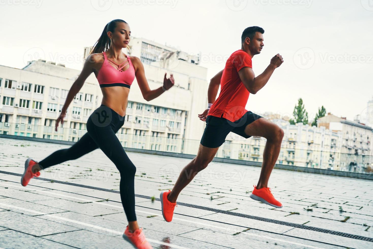 voller Länge von selbstbewussten jungen Männern und Frauen in Sportkleidung, die springen und joggen, während sie auf der Straße der Stadt im Freien trainieren foto