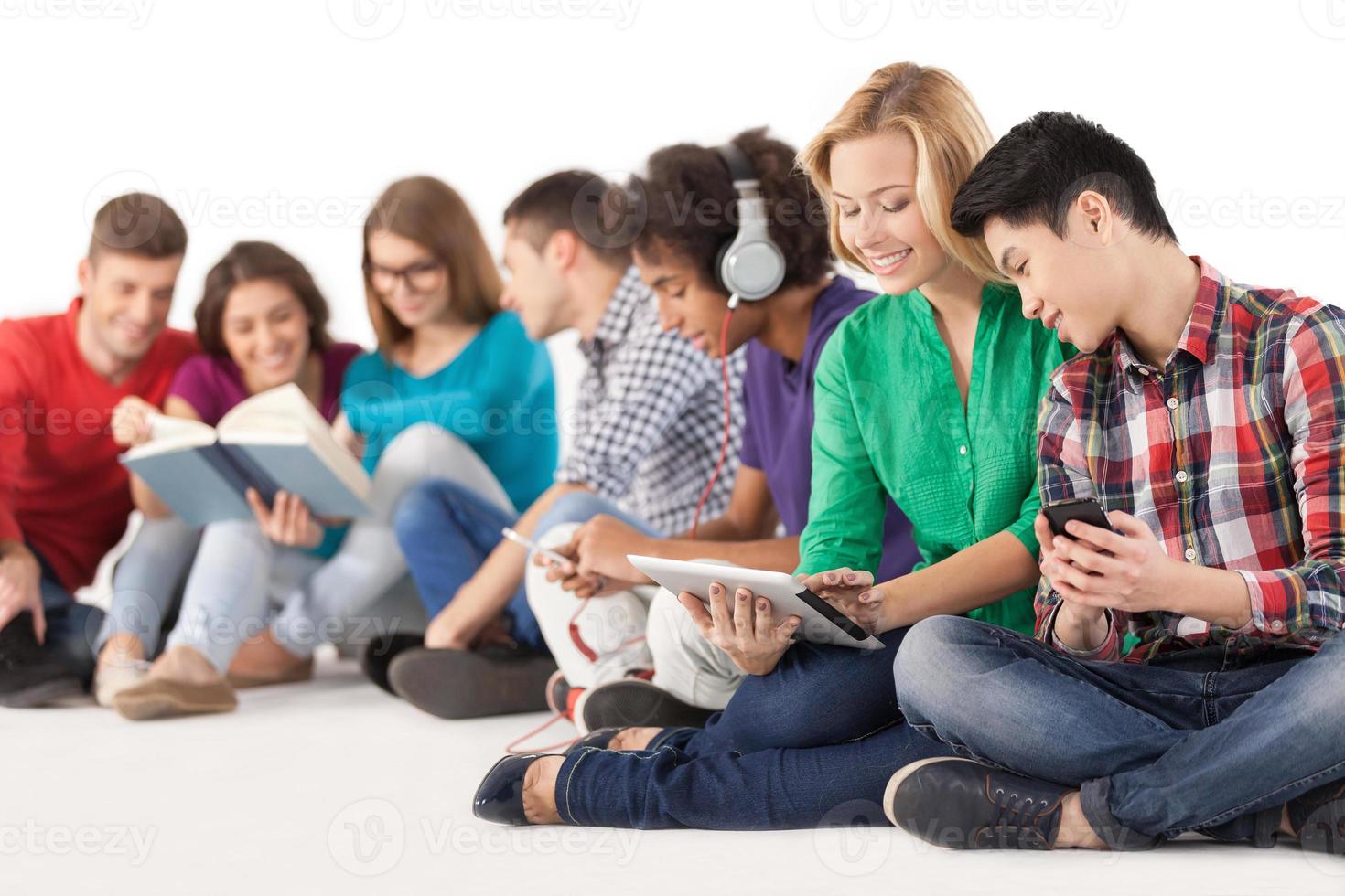 unbeschwerte Teenager. gruppe multiethnischer studenten, die zeit miteinander verbringen, während sie isoliert auf weiß sitzen foto
