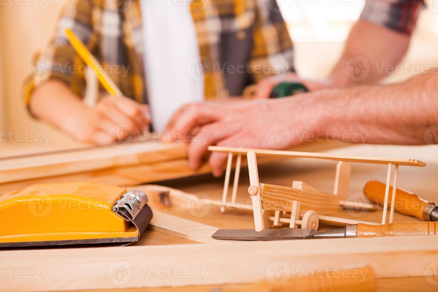 kleiner holzarbeiter, der seinen traum erschafft. nahaufnahme eines jungen männlichen tischlers, der seinem sohn beibringt, in seiner werkstatt mit holz zu arbeiten foto