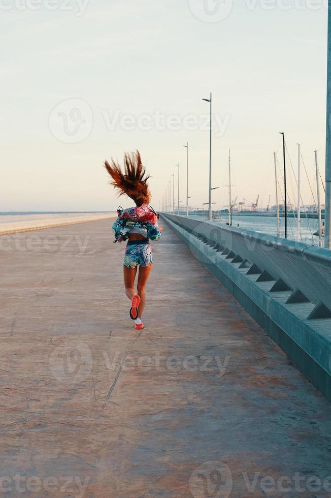 sich anstrengen. Rückansicht in voller Länge einer schönen jungen Frau in Sportkleidung, die beim Training im Freien läuft foto