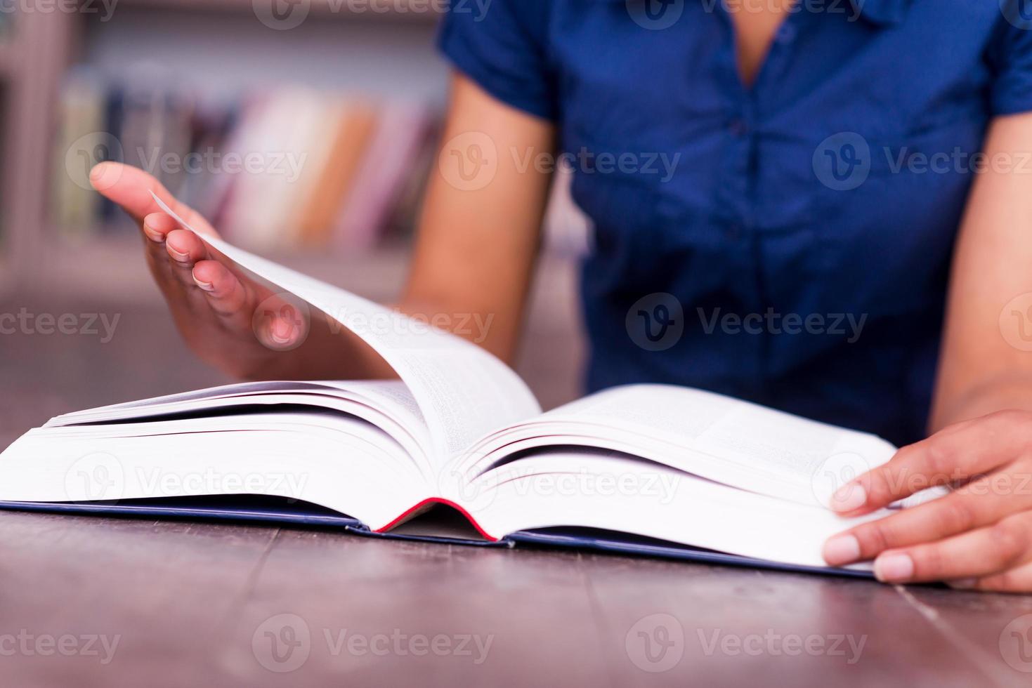 liest ihr Lieblingsbuch. Nahaufnahme einer afrikanischen Studentin, die ein Buch liest, während sie in der Bibliothek auf dem Boden liegt foto